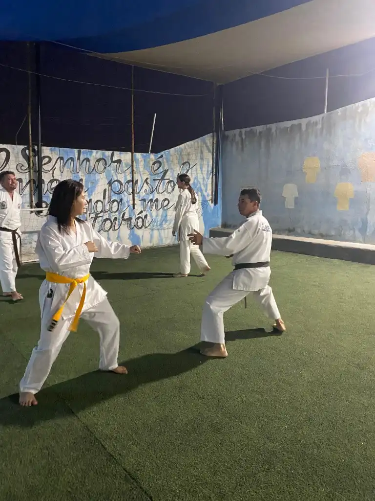 Aluna e sensei em posição de combate durante treino de karatê no gramado sintético à noite
