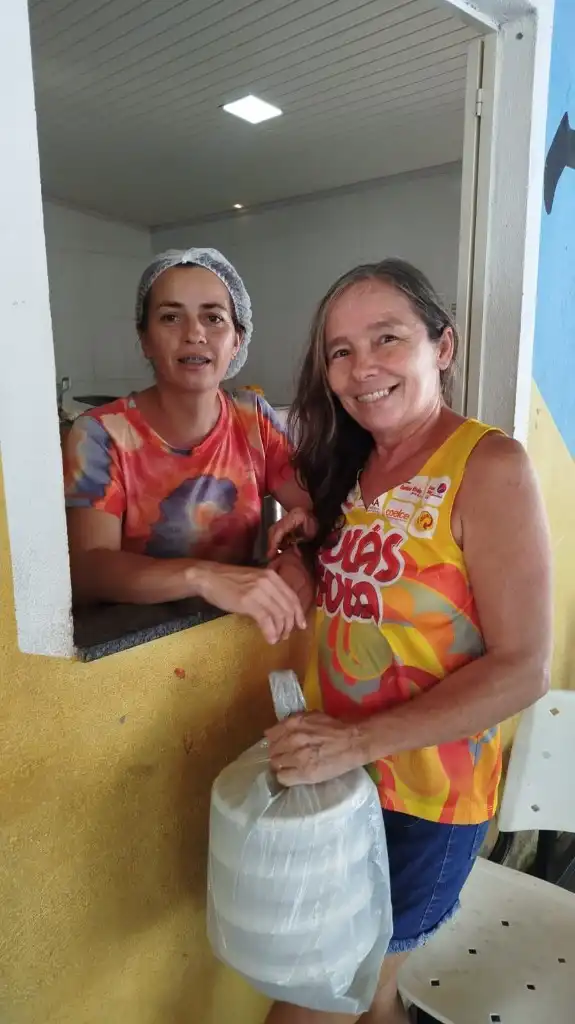 Beneficiária recebe marmitas na janela de distribuição da cozinha solidária do instituto
