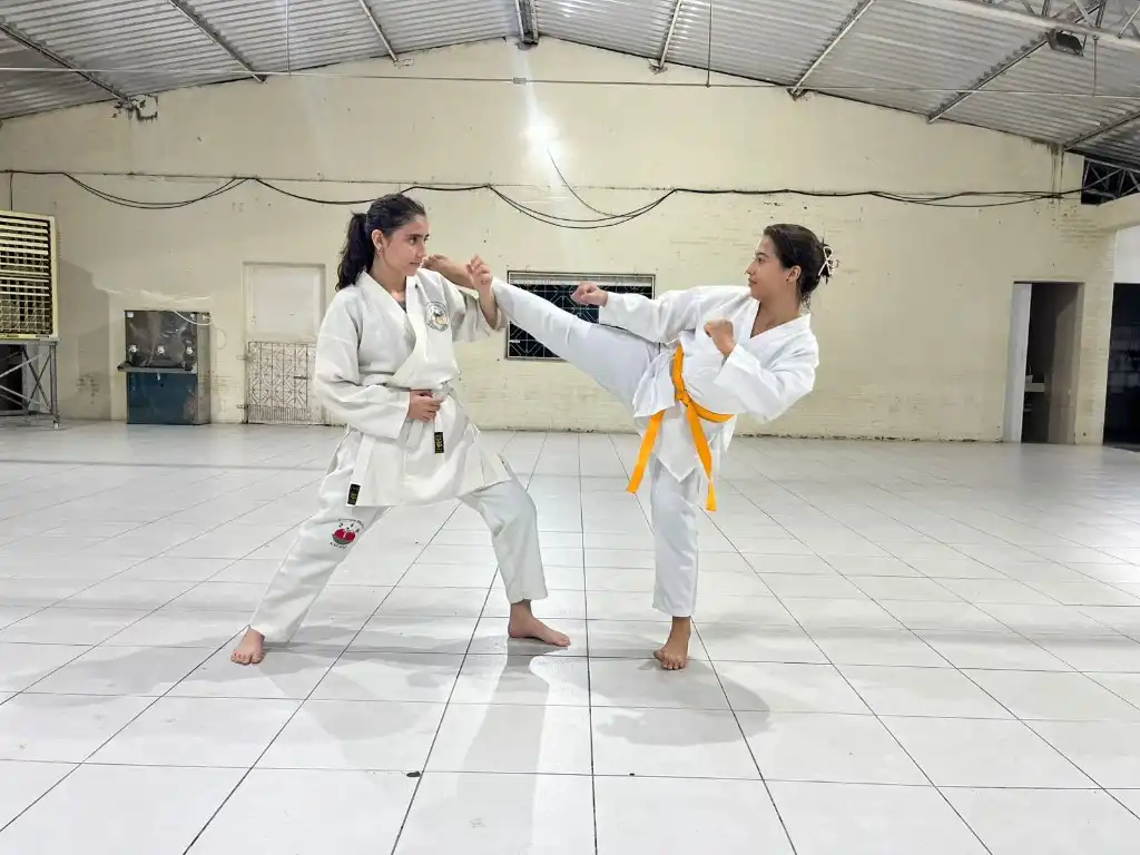 Duas jovens praticando combate controlado de karatê em sala de treino do instituto