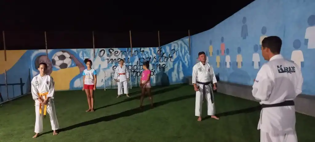 Treino noturno de karatê ao ar livre com alunos de diferentes faixas no gramado do instituto