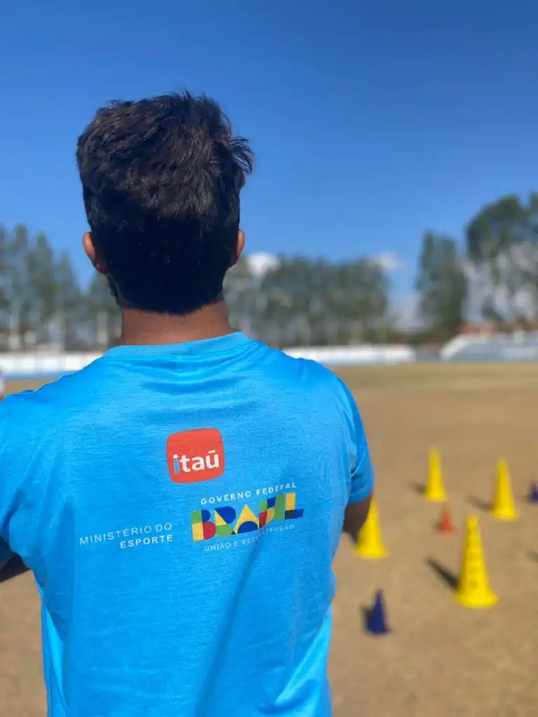Jovem atleta com uniforme da escolinha exibindo patrocínio do Itaú, Ministério do Esporte e Governo Federal no campo de treino
