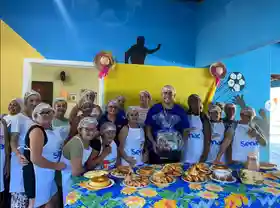 Participantes do instituto com toucas e aventais na cozinha solidária, com mesa de alimentos preparados