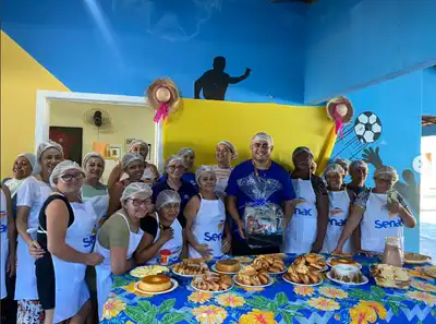 Participantes do instituto com toucas e aventais na cozinha solidária, com mesa de alimentos preparados