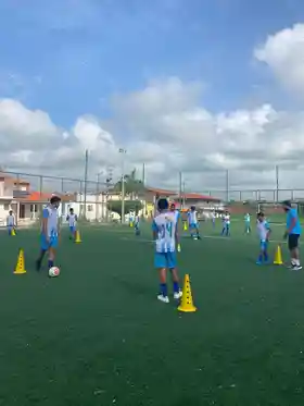 Crianças e adolescentes em treino de futebol no campo sintético do Instituto Edson Cariús, com cones e uniformes azuis